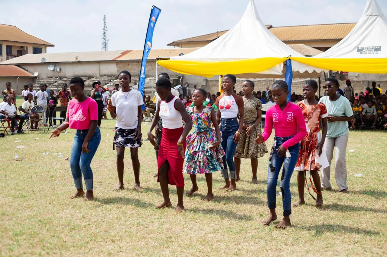 A line of girls dances barefoot on the field while other children watch from the tents.