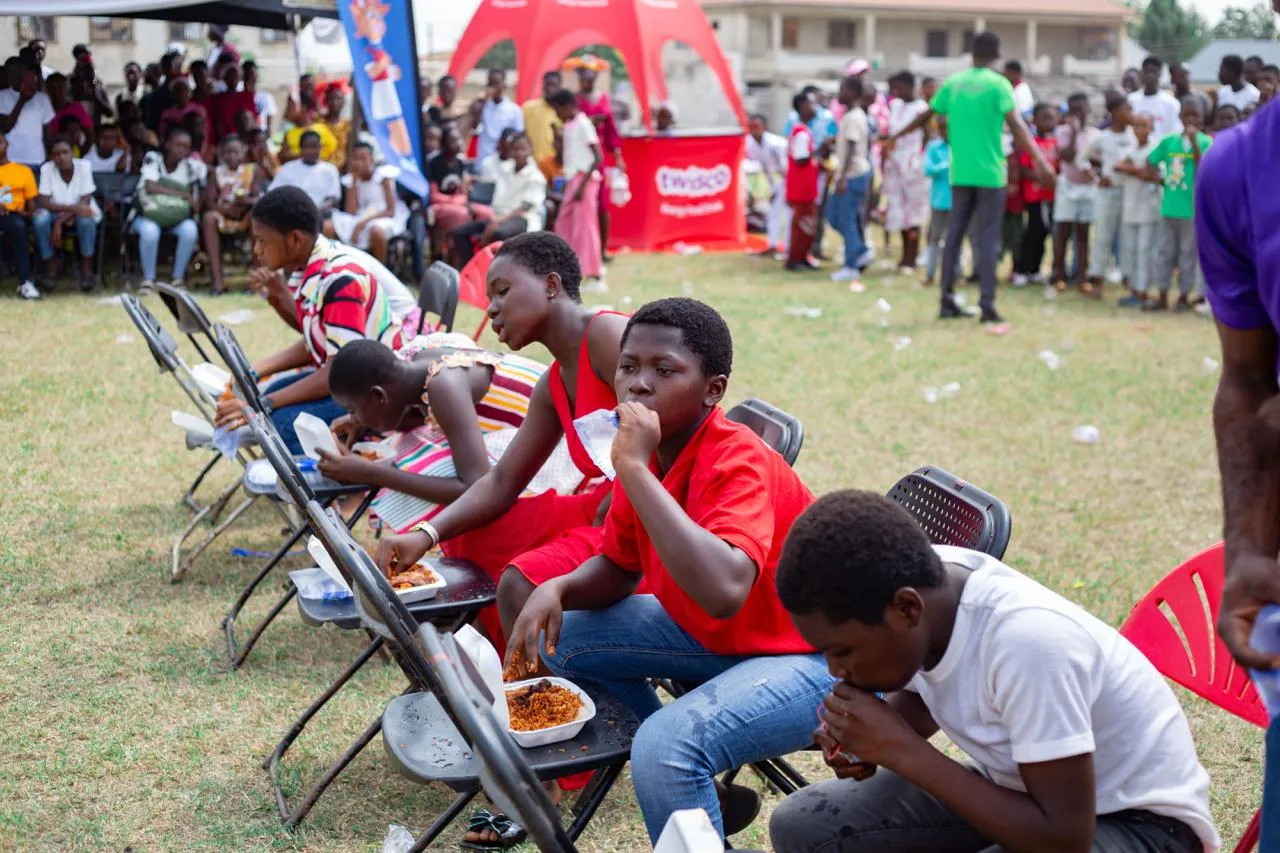 Children seated in a row take part in an eating contest with boxes of jollof rice.