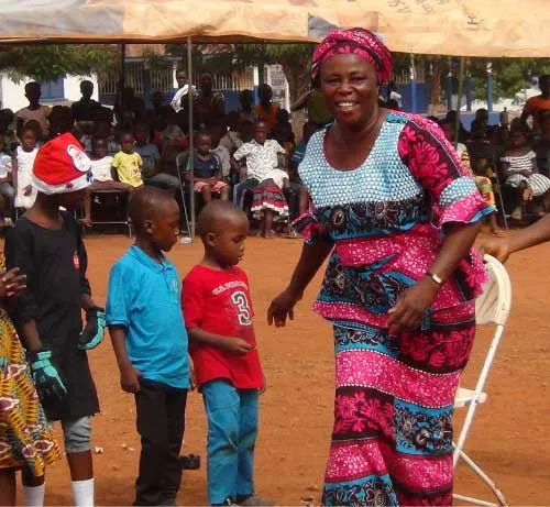 A woman dancing with children in front of a seated crowd.