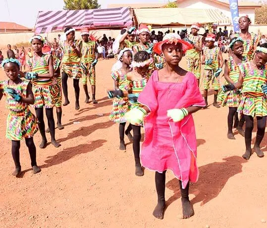 Girls in matching print outfits dancing in a line at an outdoor children’s event.