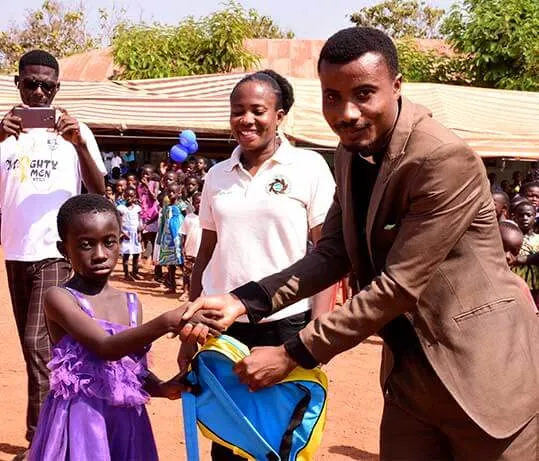 A ministry member and a guest presenting a bag to a girl in a purple dress.