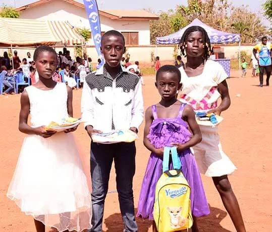 Four children in their best clothes holding plates of gifts, the youngest with a new school bag.