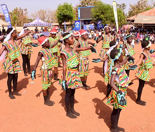 Children in print costumes dancing in formation on an open field.