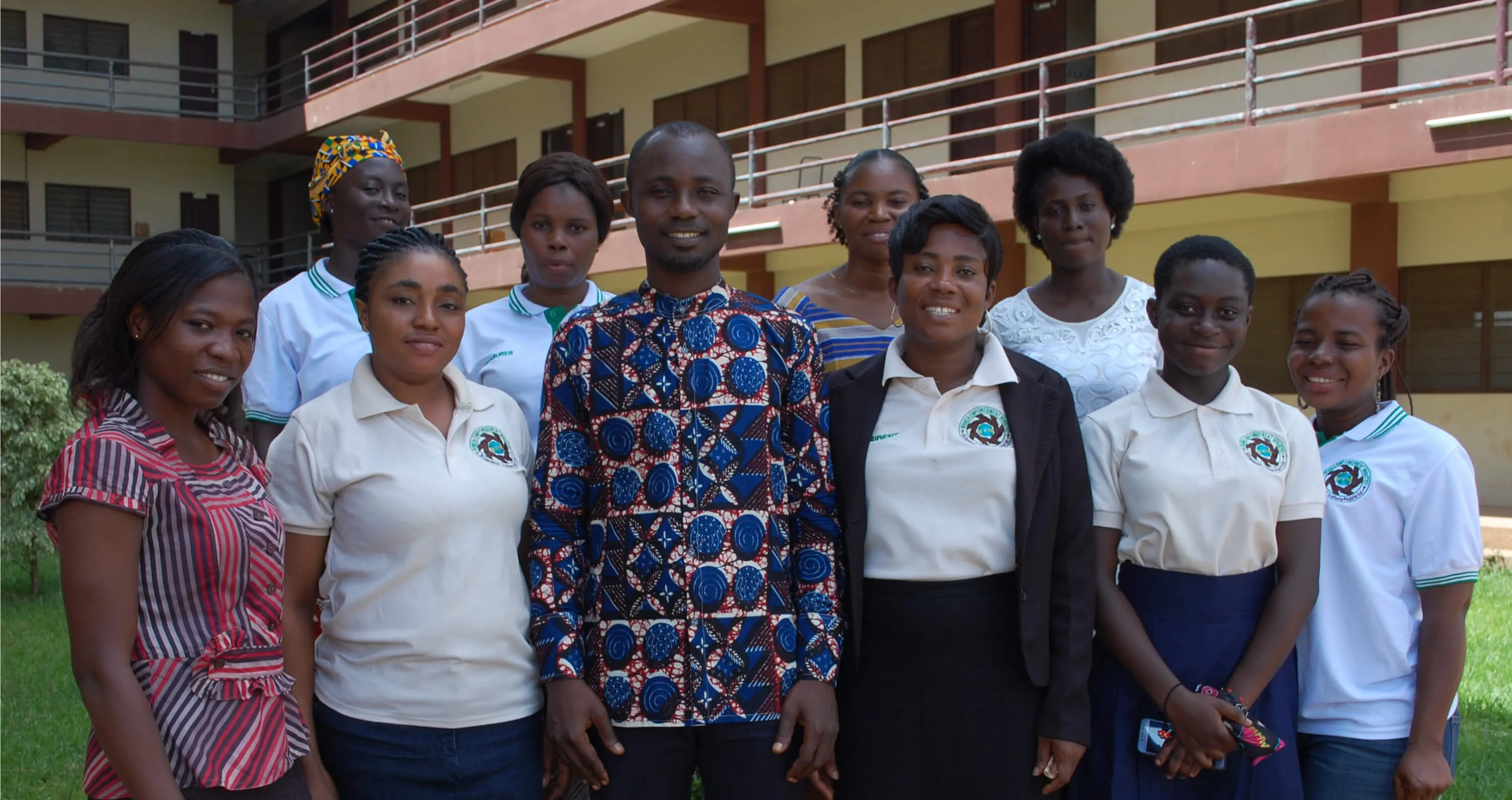 Members of Gadol Women Empowerment Ministry, most in GWEM polo shirts, standing together outside a school building.
